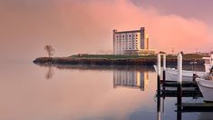 boats are docked at the dock in front of a large building and foggy sky