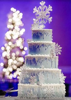 a three tiered cake with icing and snowflakes on the top is displayed in front of a christmas tree