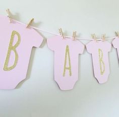 a pink banner with gold glitter letters hanging from clothes pins on a white wall,