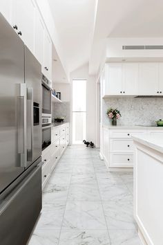 a white kitchen with marble flooring and stainless steel refrigerator freezer combos in the center