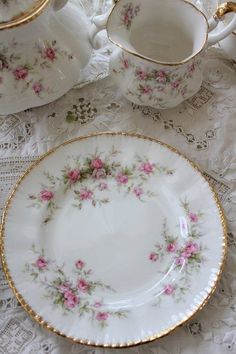 an antique china tea set with pink flowers on white lace tablecloth and gold trimmings