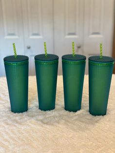 three green cups with straws in them sitting on a bed