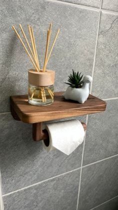 a wooden shelf with some reeds and a potted plant on it next to a toilet paper roll