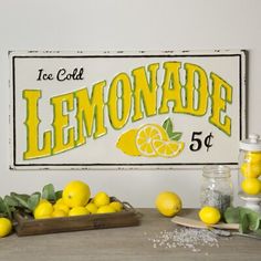 a lemonade sign sitting on top of a wooden table next to some lemons