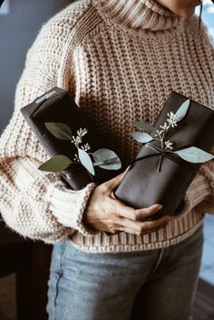 a woman holding two wrapped presents with greenery on them, both wrapped in brown paper