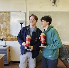 two men standing next to each other holding red cups with popcorn on top of them