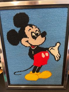 a close up of a cross stitch mickey mouse on a blue background with a silver frame