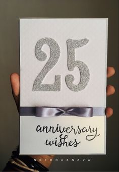 someone holding up a 25th anniversary card with the number twenty five on it and silver ribbon