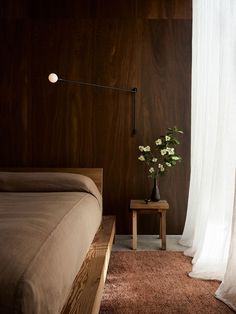 a bed sitting next to a window with curtains on both sides and a vase filled with flowers