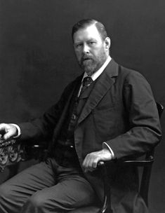 an old photo of a man in a suit and tie sitting on a chair with his arms crossed