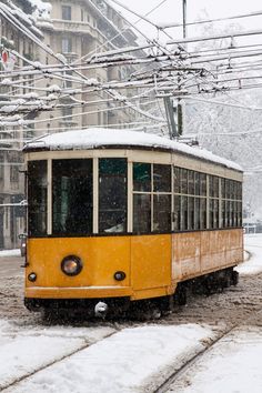 an old yellow trolley car is on the tracks in the snow, with power lines above it