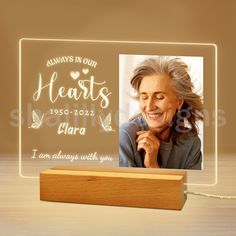 an illuminated photo frame with the words always in our hearts, and a wooden base