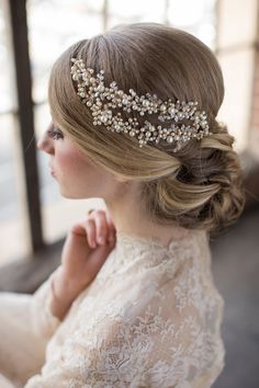 a woman wearing a bridal headpiece with pearls and beads on her hair is looking off to the side