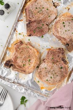 four raw pork chops on top of tin foil with parsley sprigs