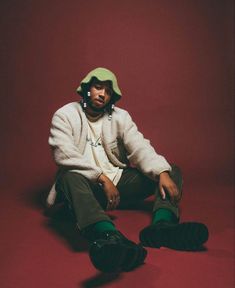 a man sitting on the ground with his feet crossed and wearing green socks, a white jacket and hat