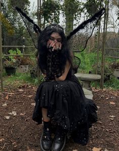 a woman dressed as a fairy sitting on a bench with her hands in her mouth