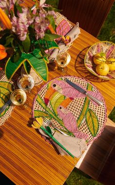 a wooden table topped with plates and bowls filled with fruit next to flowers in vases