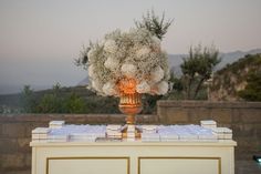 a gold vase filled with white flowers sitting on top of a table covered in books