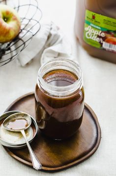 an apple cider is sitting on a plate with spoons next to the jar