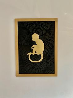 a monkey sitting on top of a black and gold framed paper cut art piece in a white walled room