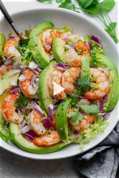 a white bowl filled with shrimp, avocado and cilantro salad on top of a table