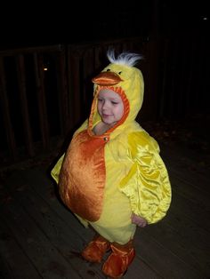 a young child dressed as a chicken standing on a wooden deck in a dark room