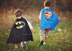 two children dressed up as batman and supermangirl walking in the grass with each other