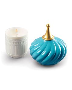 a blue candle sitting next to a white ceramic container with a gold top on it