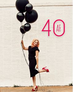 a woman is holding some black balloons in front of a white wall with the words 40 af on it