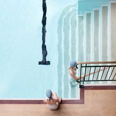 two people sitting on the edge of a swimming pool next to an umbrella and stairs