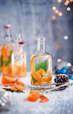 two bottles filled with liquid and orange slices on top of snow next to christmas decorations