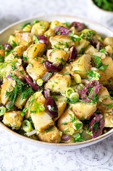 a bowl filled with potato salad and garnished with herbs, on top of a marble surface