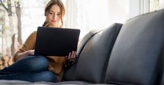 a woman sitting on a couch with a laptop computer in her hand and looking at the camera