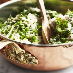 a large pot filled with rice and broccoli next to two wooden spoons