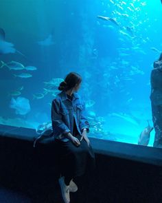 a woman sitting in front of an aquarium looking at fish