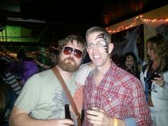 two men standing next to each other with face paint on their faces and one holding a beer