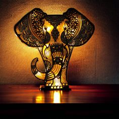 an elephant lamp is lit up on a table with a brown wall in the background