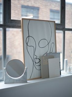 an art piece sitting on top of a window sill next to a book and mirror