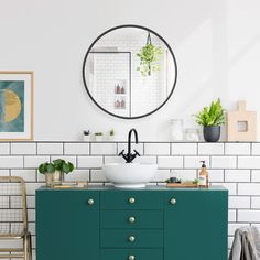 a bathroom with green cabinets and white tile on the wall, round mirror above sink