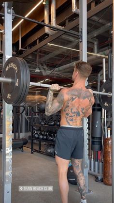 a man with tattoos is doing squats in the gym