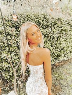 a woman in a white dress standing next to a bush