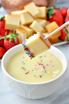 a person dipping cheese into a bowl of pudding with strawberries on the table in the background