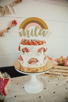 a white cake with rainbows on top sitting on a table next to a wooden sign