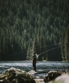 a man standing in the water while holding a fishing rod with trees in the background