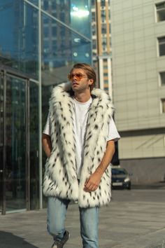 a man standing in front of a tall building wearing a white and black fur vest