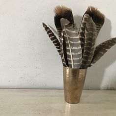 a vase filled with feathers sitting on top of a wooden table next to a wall