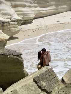 two people are sitting on rocks in the water at the beach and one person is kissing the other