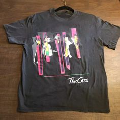 a black t - shirt with the words the cars on it sitting on a wooden floor