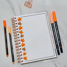 an open notebook with three markers and two pencils next to it on a marble surface