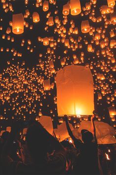 many people are releasing lanterns into the sky at night time with their hands in the air